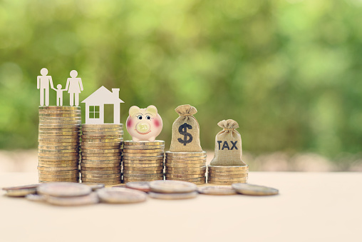 Estate Assets Concept: Family couple, home model, piggy bank, dollar and tax bags on stacks of rising coins