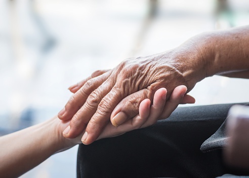 Special Needs Beneficiary concept: close up of young hand holding the hand of an elderly person