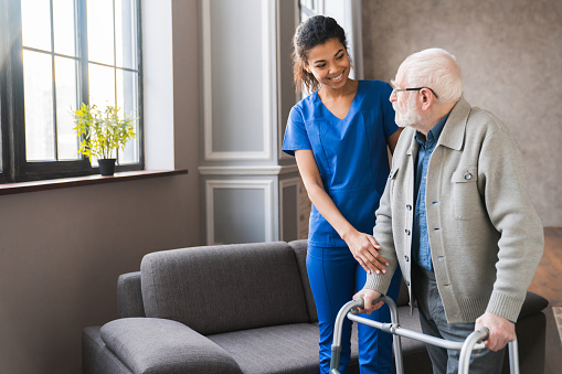 Aging in place concept: elderly man with using a walker is being helped by a nurse