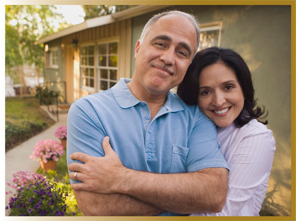 Middle aged husband and wife standing in front of their home