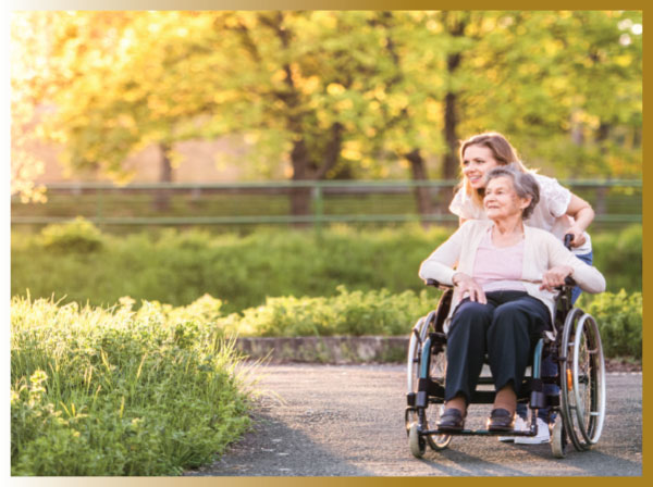 Young adult daughter pushing her over 65 year mother's wheelchair on a path