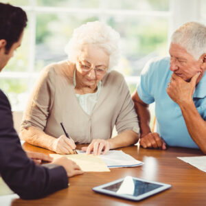 Over 65 year old husband and wife signing estate planning documents with their attorney in their home.